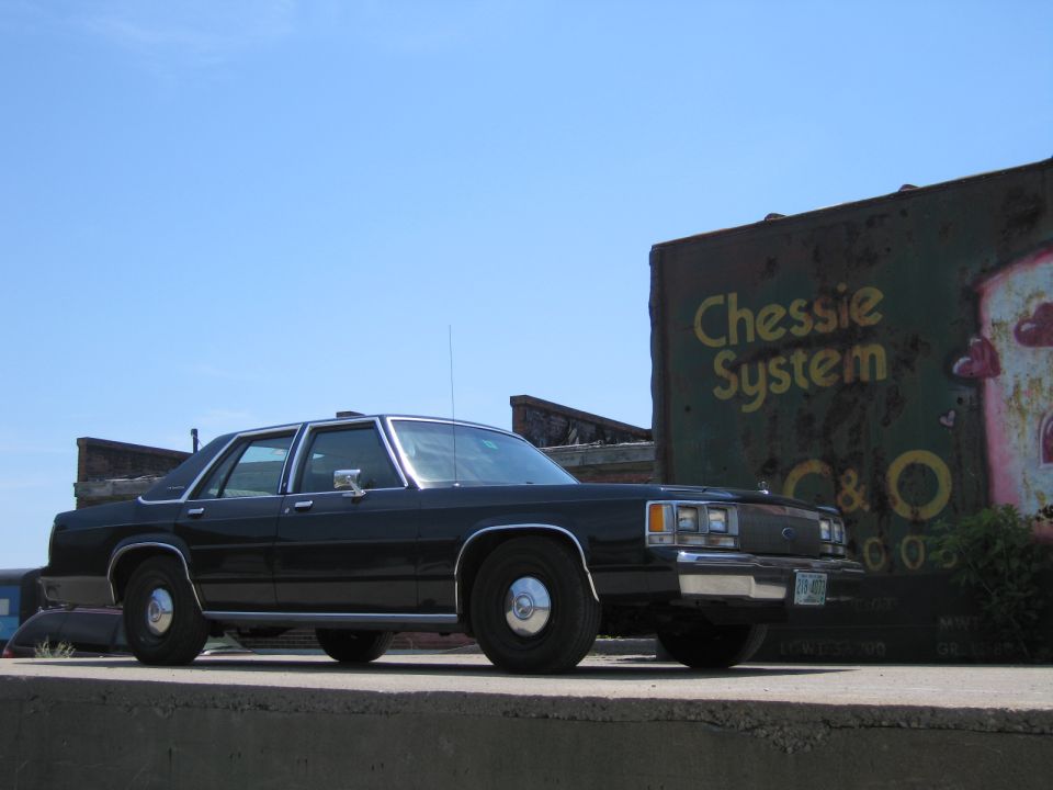 Front view of a black Ford LTD Crown Victoria beside a Chessie System boxcar