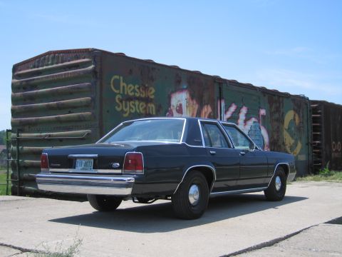 2001 Ford Crown Victoria - Photograph of a black Ford LTD Crown Victoria parked beside a graffiti-covered Chessie System boxcar.