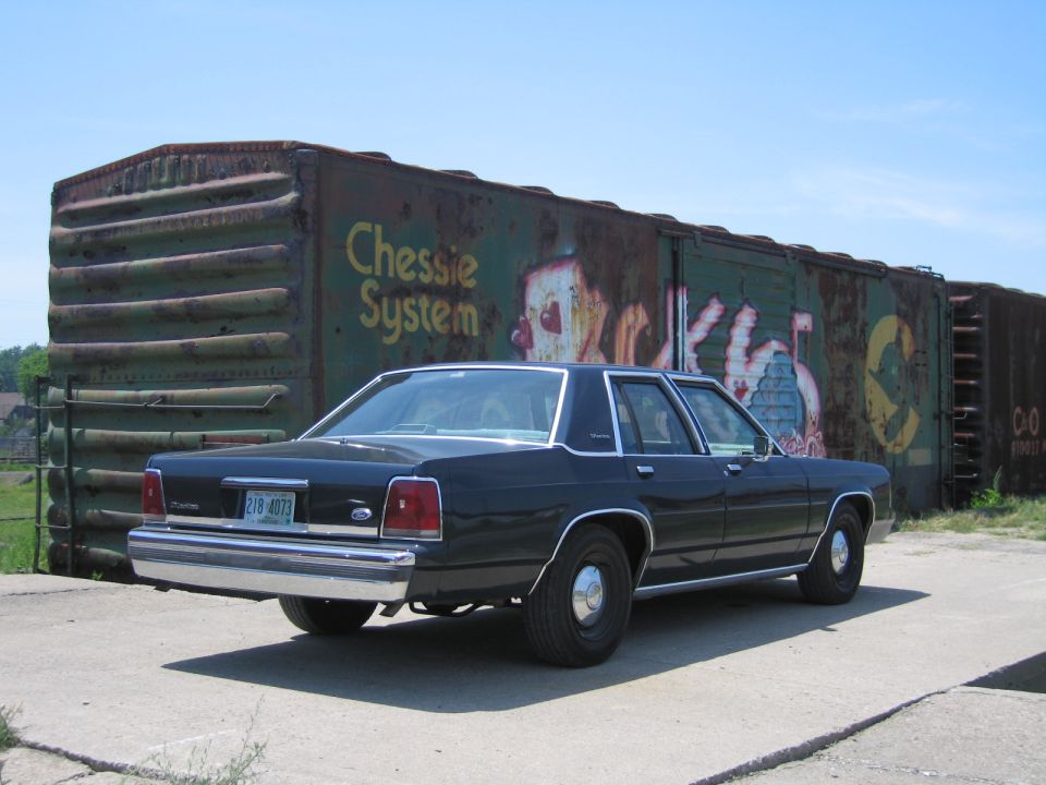 Rear three-quarter view of a black Ford LTD Crown Victoria by a Chessie System boxcar