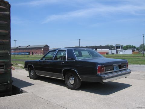2001 Ford Crown Victoria - Photograph of a black Ford LTD Crown Victoria sedan parked beside railroad equipment in a railyard.
