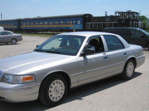 2001 Ford Crown Victoria - Photo of a silver Ford Crown Victoria sedan in front of railcars, not a technical document.