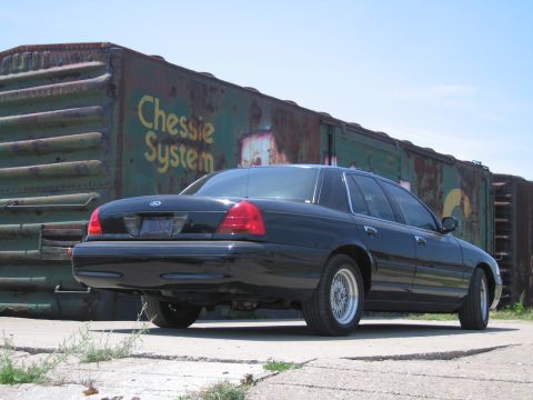 2001 Ford Crown Victoria - Photo of a black Ford Crown Victoria parked by a Chessie System boxcar, not a technical document.