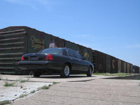 2001 Ford Crown Victoria - Photo of a black Ford Crown Victoria next to a line of boxcars, not a technical document.