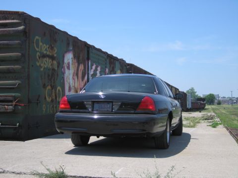2001 Ford Crown Victoria - Photo of a black Ford Crown Victoria by graffitied boxcars, not a technical document.