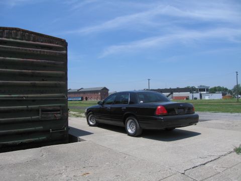 2001 Ford Crown Victoria - Photo of a black Ford Crown Victoria beside a rusted boxcar, not a technical document.