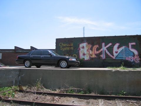 2001 Ford Crown Victoria - Photo of a black Ford Crown Victoria above tracks by a graffiti boxcar, not a technical document.