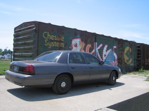 2001 Ford Crown Victoria - Photo of a gray Ford Crown Victoria by a graffitied boxcar, not a technical document.