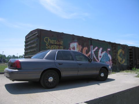 2001 Ford Crown Victoria - Photo of a gray Ford Crown Victoria by a graffitied boxcar, not a technical document.