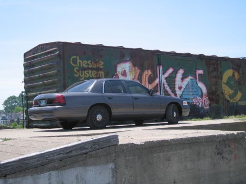 2001 Ford Crown Victoria - Photo of a gray Ford Crown Victoria near a graffitied boxcar, not a technical document.