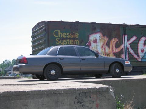 2001 Ford Crown Victoria - Photo of a gray Ford Crown Victoria by a graffitied boxcar, not a technical document.