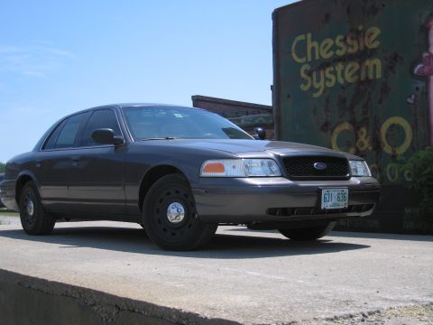 2001 Ford Crown Victoria - A dark gray 2001 Ford Crown Victoria is seen from the front-right angle, parked next to a weathered C&O System sign.