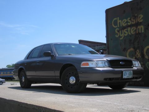 2001 Ford Crown Victoria - This dark sedan, seen from the front 3/4 angle, matches the description of a 2001 Ford Crown Victoria.