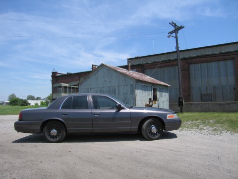2001 Ford Crown Victoria - A gray 2001 Ford Crown Victoria is parked outdoors in front of industrial buildings.