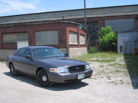 2001 Ford Crown Victoria - A 2001 Ford Crown Victoria sedan is seen parked outdoors in front of an industrial-style brick building.