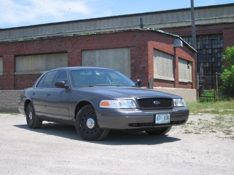 2001 Ford Crown Victoria - A 2001 Ford Crown Victoria is parked outside an industrial brick building on a sunny day.