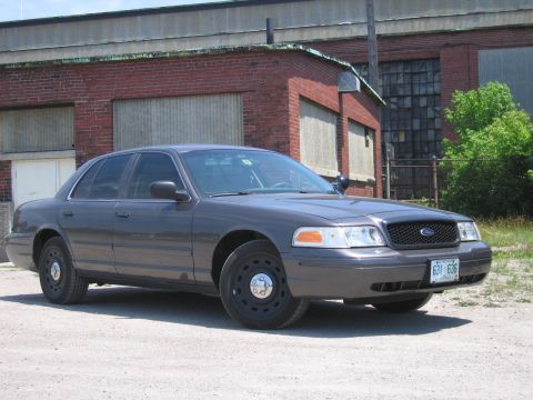 2001 Ford Crown Victoria - A gray 2001 Ford Crown Victoria is parked in front of an industrial brick building.