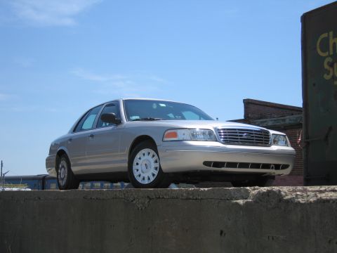 2001 Ford Crown Victoria - A silver 2001 Ford Crown Victoria is parked on a concrete barrier with a building in the background.