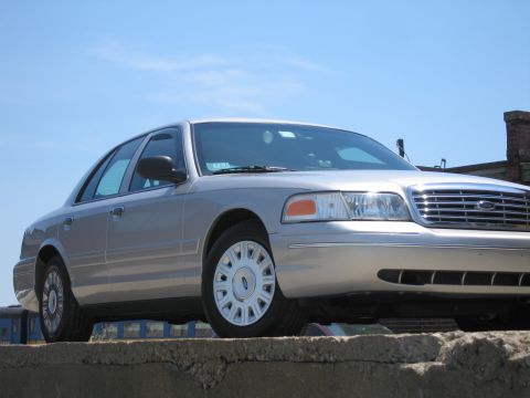 2001 Ford Crown Victoria - A silver 2001 Ford Crown Victoria sedan is parked on a concrete barrier under a clear blue sky.