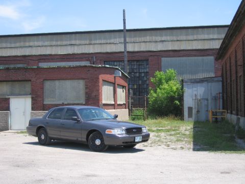 2001 Ford Crown Victoria - A dark gray 2001 Ford Crown Victoria is parked in an industrial area with a brick building in the background.
