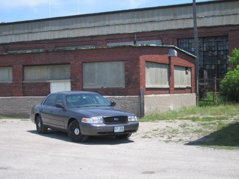 2001 Ford Crown Victoria - A gray 2001 Ford Crown Victoria sedan is parked in front of an industrial brick building.