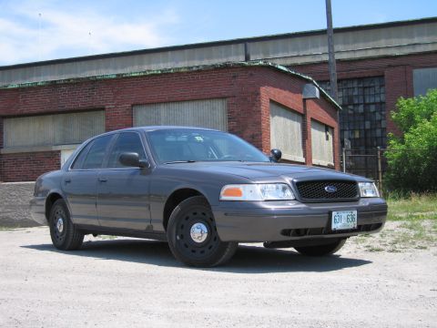2001 Ford Crown Victoria - A gray 2001 Ford Crown Victoria police car is parked outside a brick building under a blue sky.