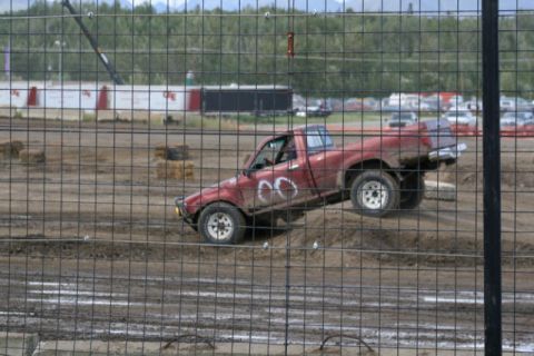 1975 Toyota Land Cruiser - A red pickup truck navigates a muddy track, its wheels kicking up dirt.