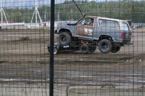 1975 Toyota Land Cruiser - A modified SUV is driven on top of another vehicle during an event on a dirt track.