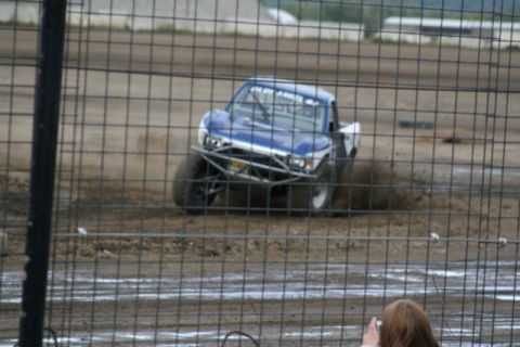 1975 Toyota Land Cruiser - A modified truck competes on a dirt track, obscured by a wire fence.