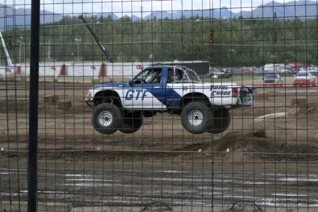 Pickup truck with "GTF" and "TOTAL CHAOS" graphics airborne over dirt track