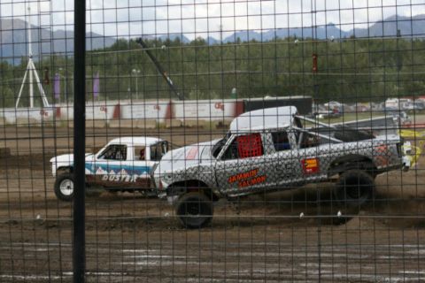 1975 Toyota Land Cruiser - Modified pickup trucks compete on a dirt track, with one vehicle displaying 'DUSTER' and the other 'JAMMIN SALMON'.