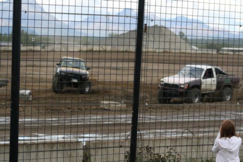 1975 Toyota Land Cruiser - Modified trucks compete on a dirt track, with mountains in the background and a spectator watching.