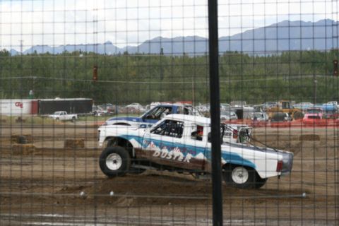 1975 Toyota Land Cruiser - Modified pickup trucks compete on a dirt track, with mountains visible in the distance.