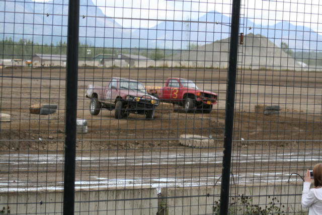 Two pickup trucks racing on a dirt track, one red with number 3, one maroon