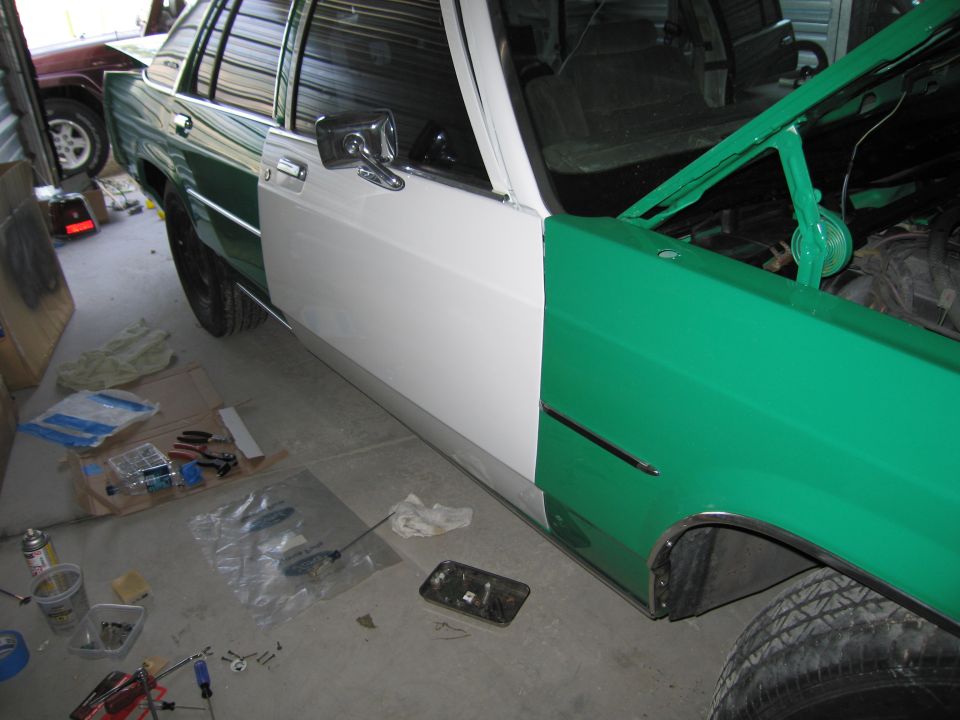 Car with green and white two-tone paint, hood open, side view. Tools and parts scattered on the floor