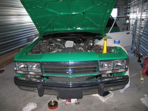 1991 Ford LTD Crown Victoria - The front of a green Ford Crown Victoria is shown with its hood open, revealing the engine compartment.