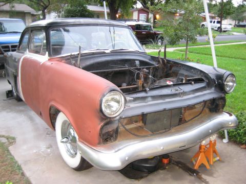 1953 Ford Mainline - A 1950s Ford two-door sedan mid-restoration in a driveway, two-toned in red-oxide primer and black with the front clip stripped and hood re…