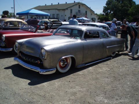 1953 Ford Mainline - A 1953 Ford Mainline sedan, unfinished but with distinctive whitewall tires and chrome accents, sits parked at an outdoor event.