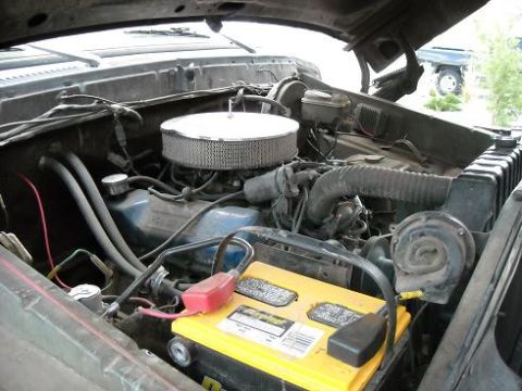 1978 Ford Bronco - The engine bay of a 1978 Ford Bronco, a prominent yellow battery and chrome air filter, with another vehicle visible in the background.