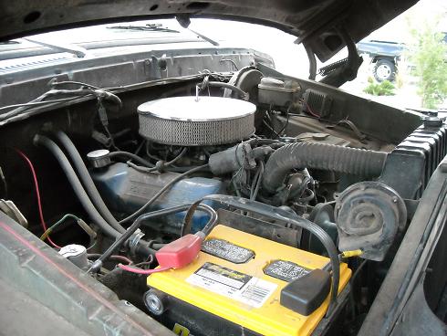 Engine bay of a 1978 Ford Bronco with a yellow battery and chrome air filter
