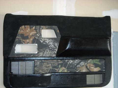 1978 Ford Bronco - A black car door panel with camouflage accents and a chrome-trimmed window crank hole is shown.