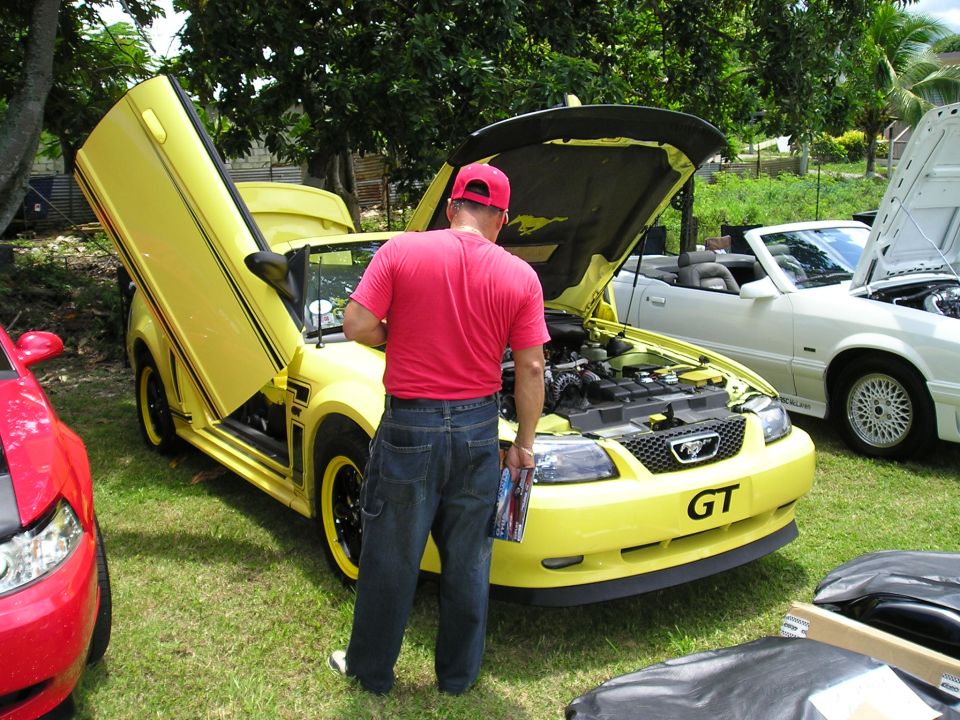 Yellow Mustang convertible with doors open, a guy looking at the engine. White convertible in background