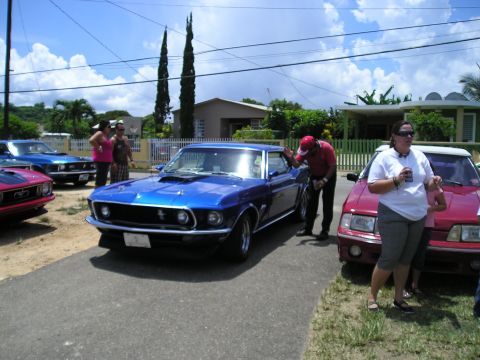 2009 Ford Mustang - A group of people admire a classic blue Ford Mustang parked on a sunny day.