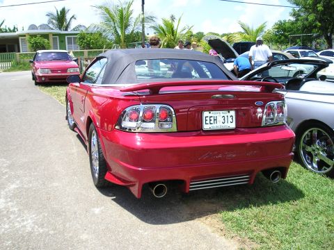 2009 Ford Mustang - A red convertible Mustang is parked next to other vehicles, showing its rear end and license plate.