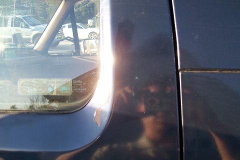 1988 Ford Bronco - Close-up of a dark vehicle's side mirror and door panel, with other cars seen through the window.