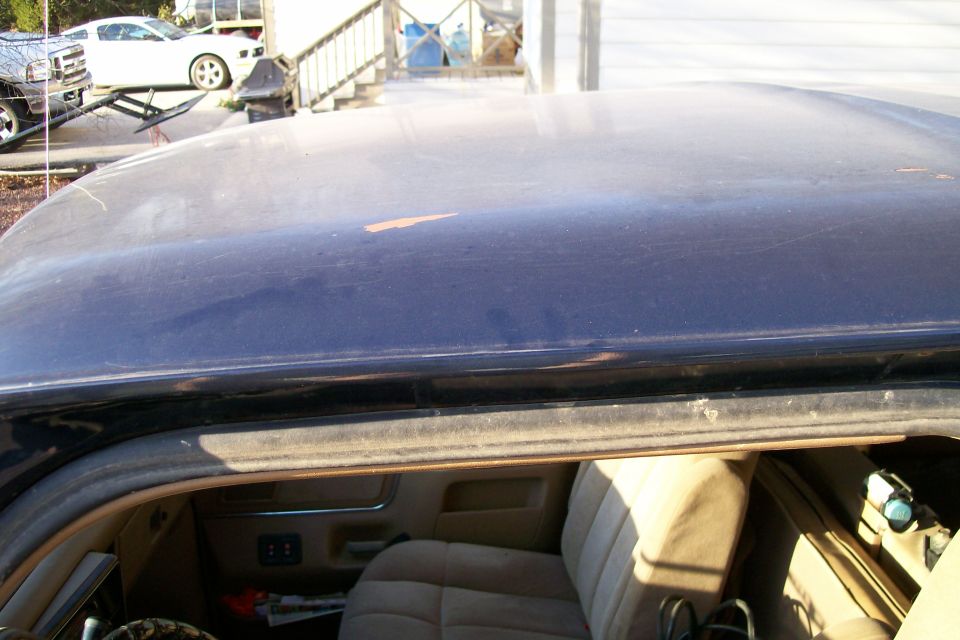 Dark blue truck roof with paint chips, door open showing tan cloth seats and door panel