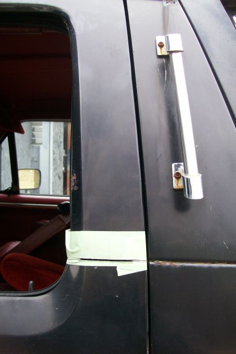 1988 Ford Bronco - Close-up view of a vehicle's interior door frame, showing tape and a chrome handle.