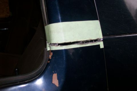 1988 Ford Bronco - Masking tape covers a cut line on a dark blue vehicle body panel, suggesting modification or repair.