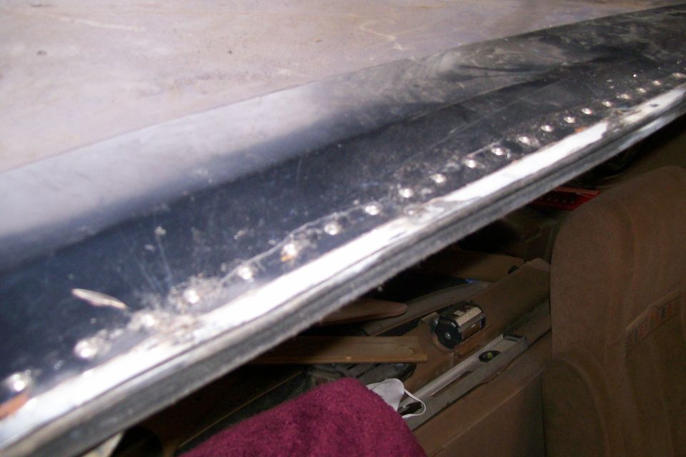 Row of ground-down welds along the lower seam of a dark body panel during repair
