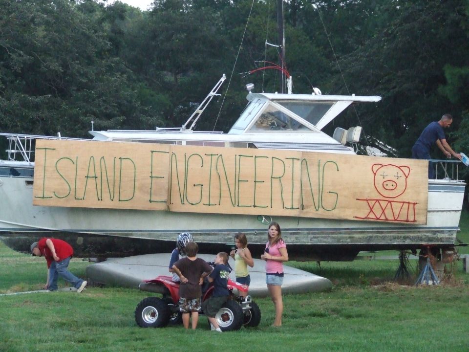 Boat with sign "ISLAND ENGINEERING" and a pig drawing, people and ATV in front.