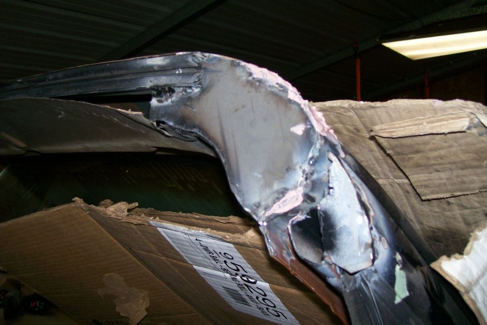 Curved welded metal body panel resting on cardboard in a shed